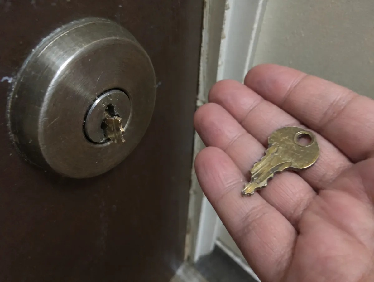 Mitad de una llave rota en la mano junto a la cerradura donde ha quedado el otro trozo