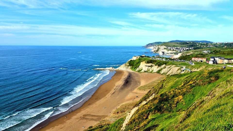 Playa de arena bajo los acantilados verdes de Sopelana